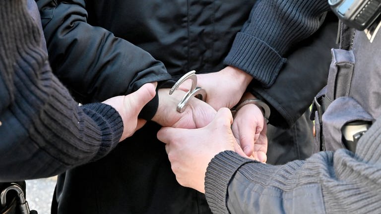 Polizisten legen einem Festgenommenen Handschellen an.